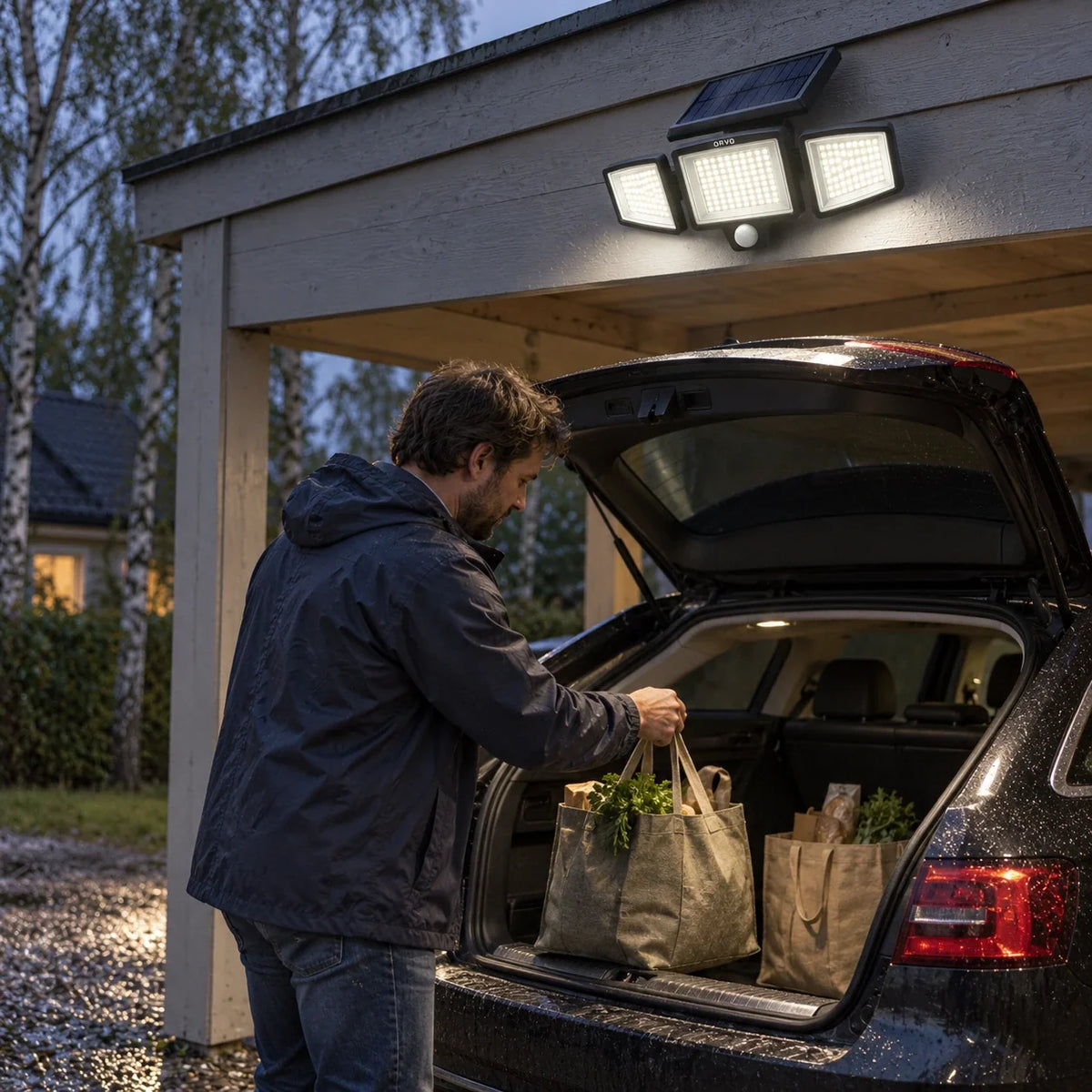 En man lastar ur matkassar ur bilen under en tänd Orvo solcellslampa i en carport